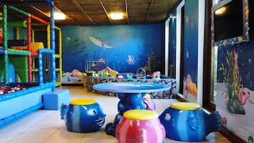 Espaço de recreação interno com mesa de bilhar, banquinhos coloridos e um mural com tema de fundo marinho.