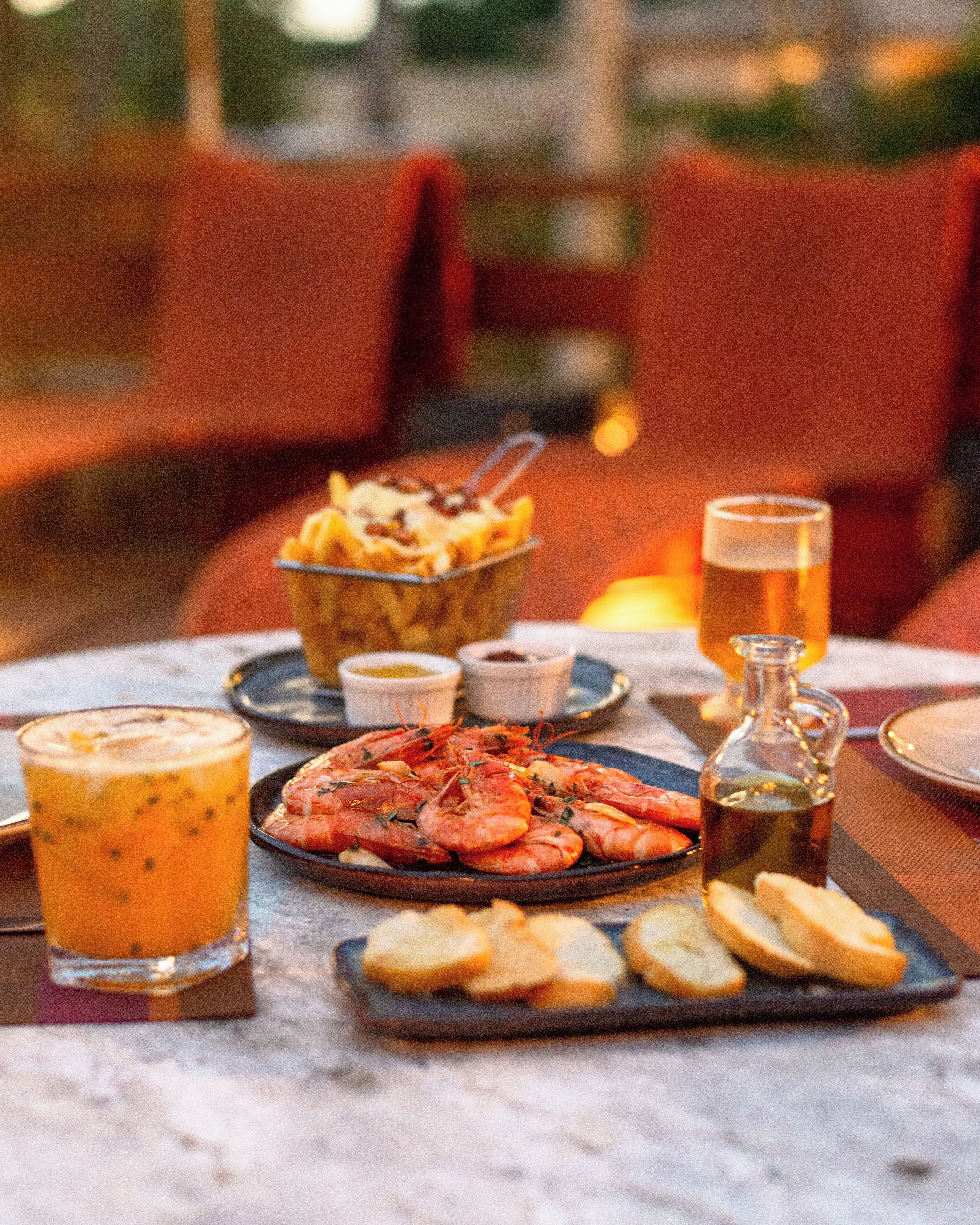 A dining table with seafood dishes, a beer glass, and a bottle of olive oil.