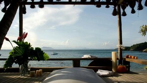 A wooden deck with a view of the sea, a massage table, candles, and a potted plant. - Hotel La Foret & Beach Club (Búzios)