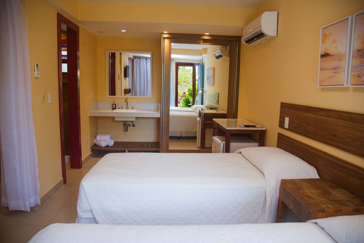 Habitación de hotel con dos camas, baño con espejo, lavabo y toallero.
