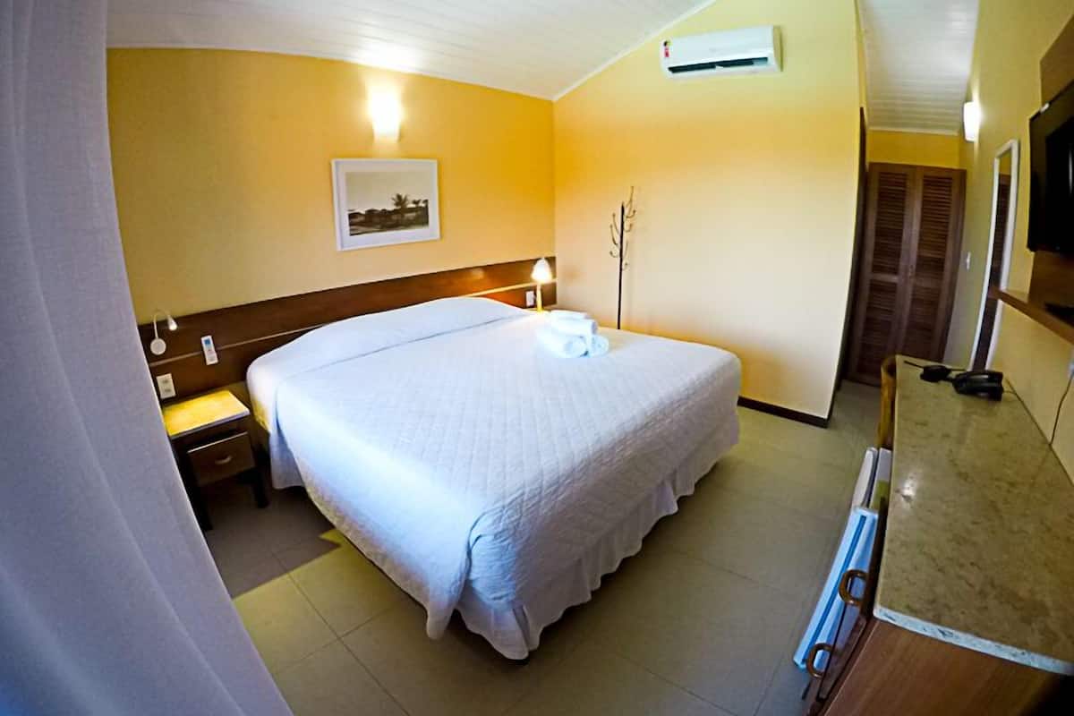 Una habitación de hotel con una cama grande, una mesita de noche, una lámpara, aire acondicionado y un espejo.
