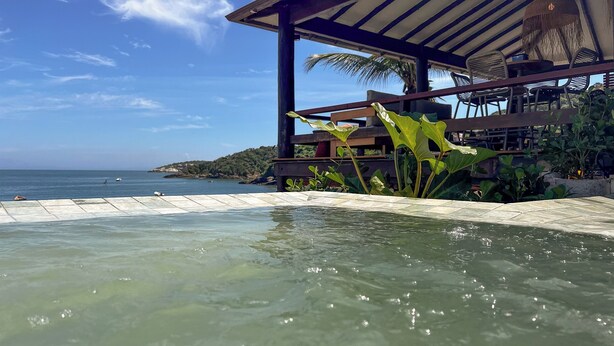 A pool area with clear water, a wooden deck, and a view of the sea. - Hotel La Foret & Beach Club (Búzios)