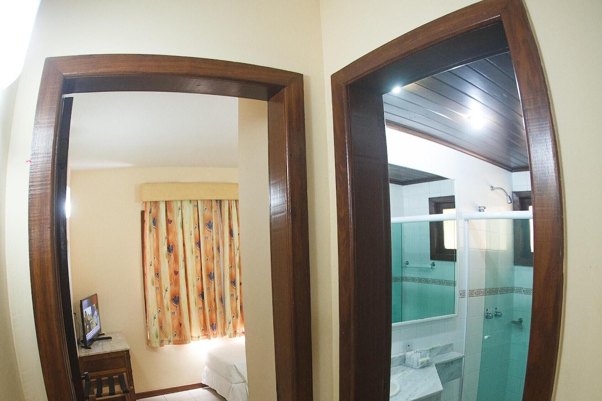 Una habitación con escritorio, cama, ducha y baño con espejo.
