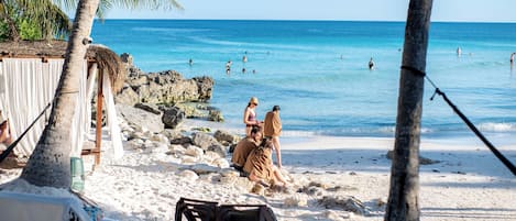 Una playa con palmeras, una cabaña de techo de paja y una orilla arenosa.