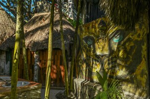 Une hutte au toit de chaume, avec un banc en pierre et une grande fresque représentant le visage d’un léopard.