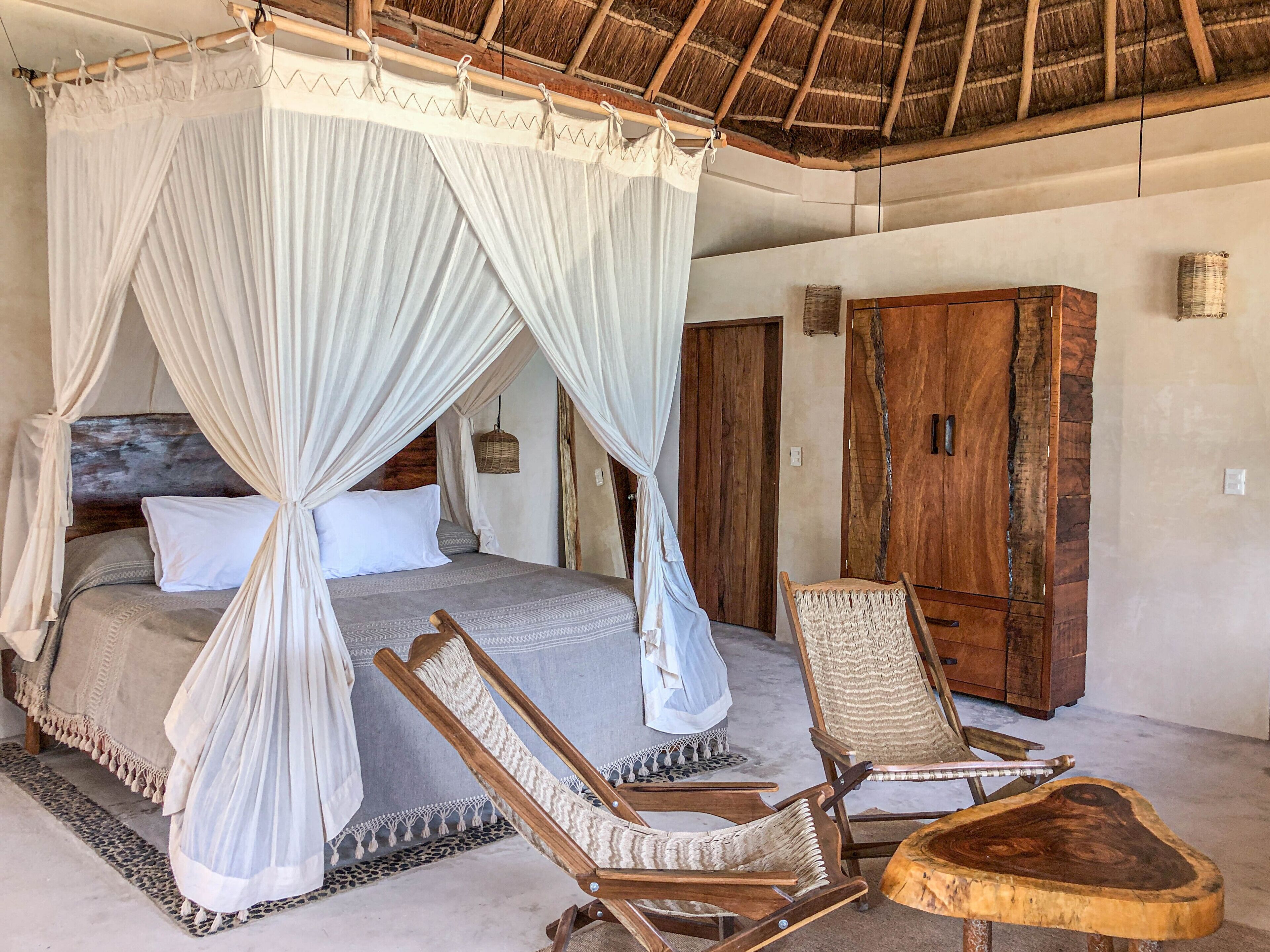 A bedroom with a four-poster bed, wooden furniture, and a thatched roof.