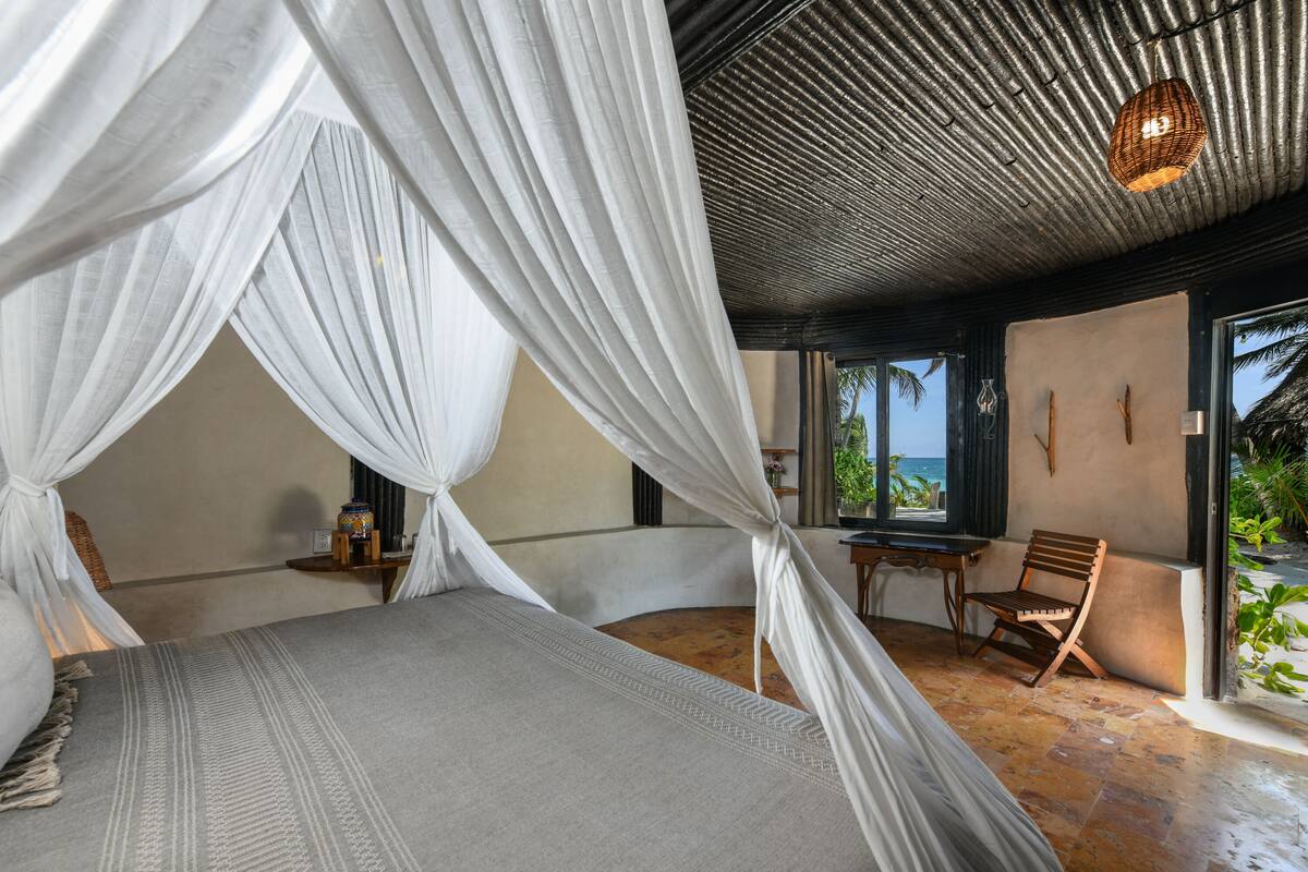 A bedroom with a bed, a chair, a table, and a view of the ocean.