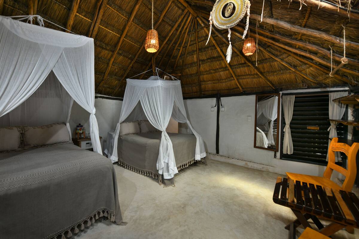 A room with two beds, each with a canopy, a hanging light fixture, and a mirror on the wall.