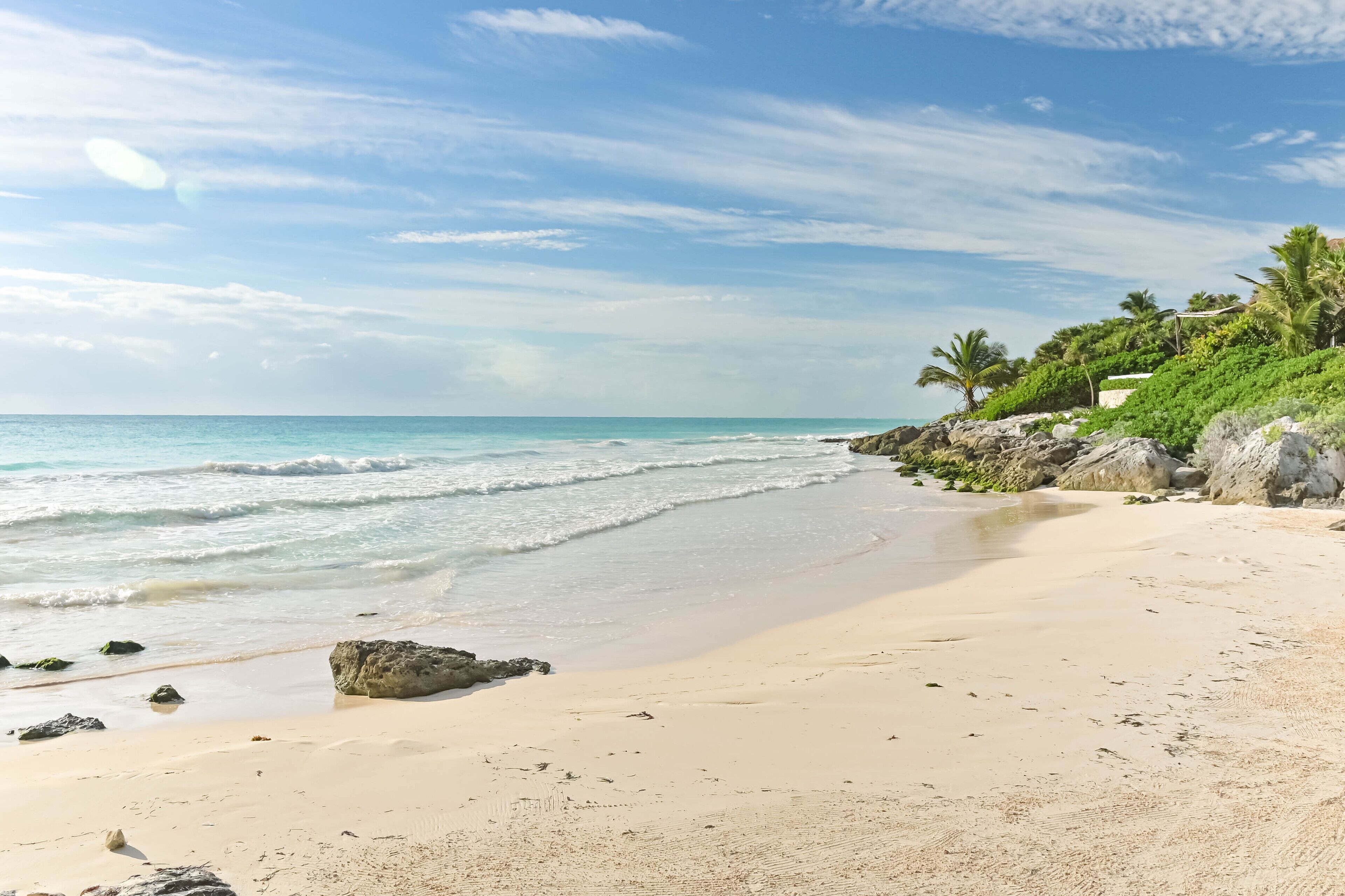 A beach with clear skies, calm waves, and rocky outcrops.
