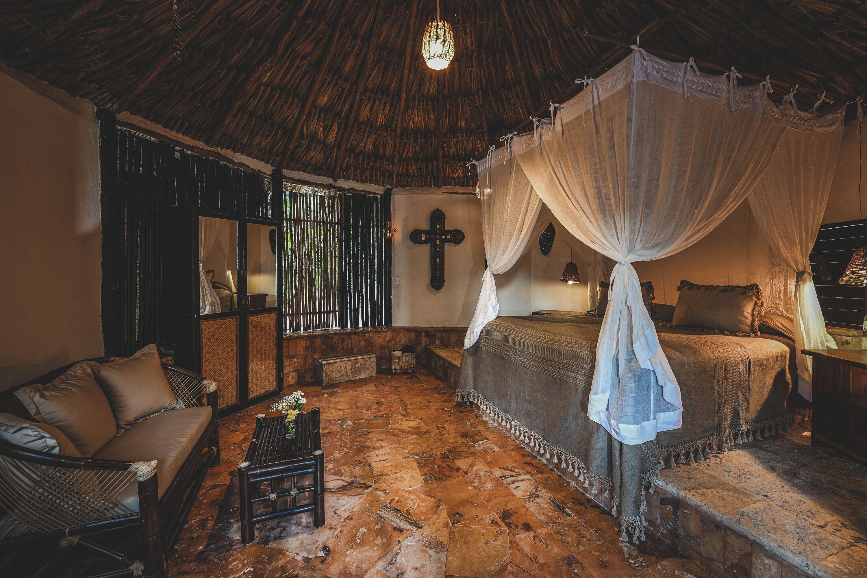 A room with a bed under a canopy, a sofa, a small table, and a cross on the wall.