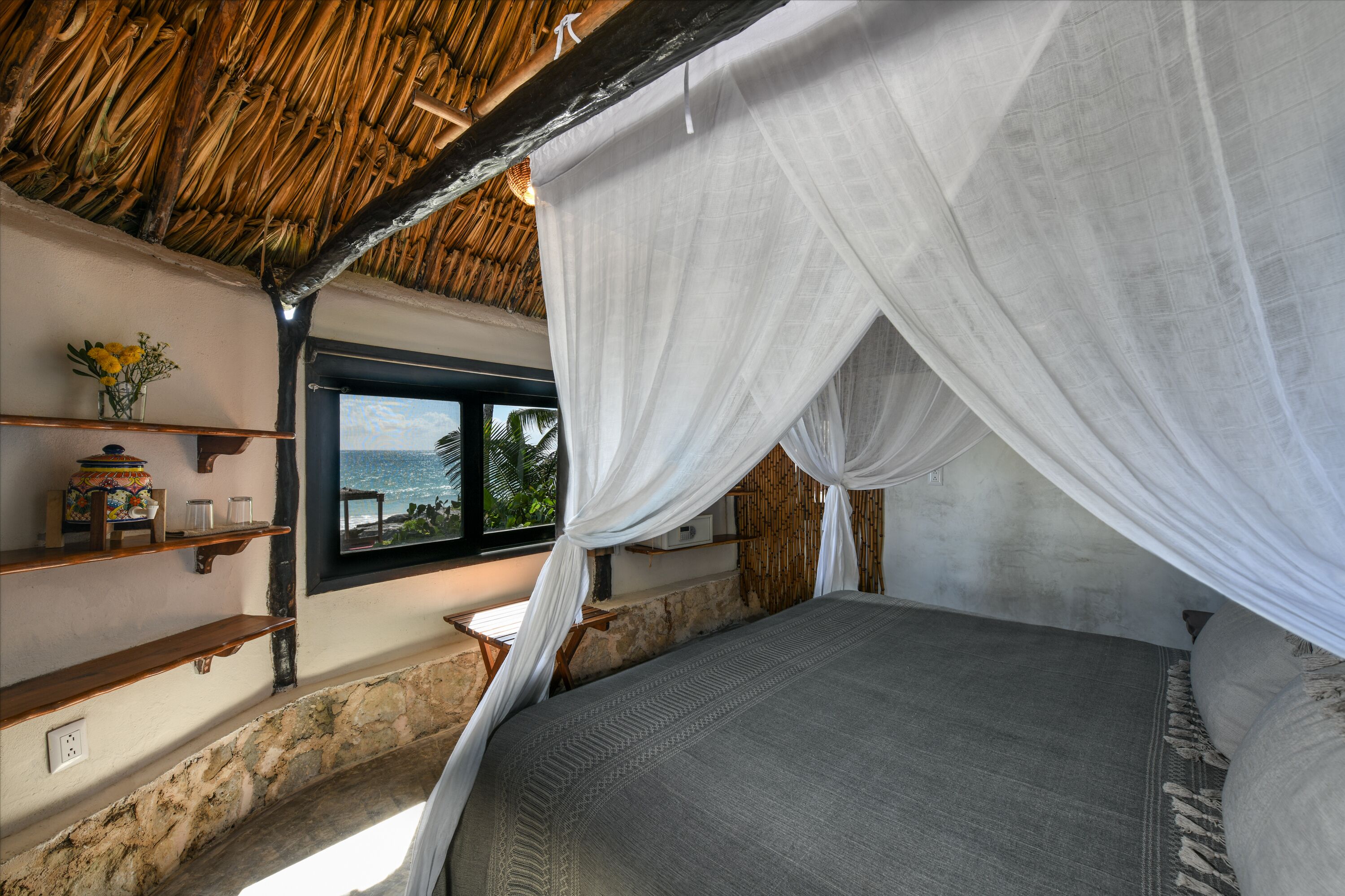 A room with a bed under a canopy, a window with a view, and shelves with items.