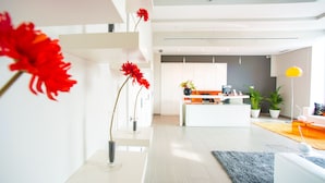 A modern living room with a sofa, a coffee table, and a rug. There is a kitchen area in the background with a counter and plants. - Ona Living Barcelona (L'Hospitalet de Llobregat)