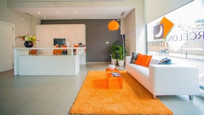 A modern living room with a white sofa, orange rug, and a kitchen area in the background. - Ona Living Barcelona (L'Hospitalet de Llobregat)