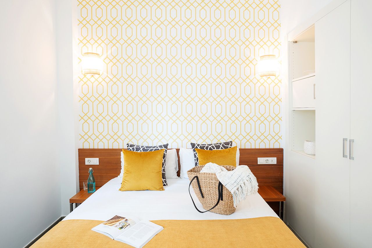 Une chambre d’hôtel comprenant un lit, des tables de chevet, une lampe, un mur orné d’un motif géométrique et une armoire.