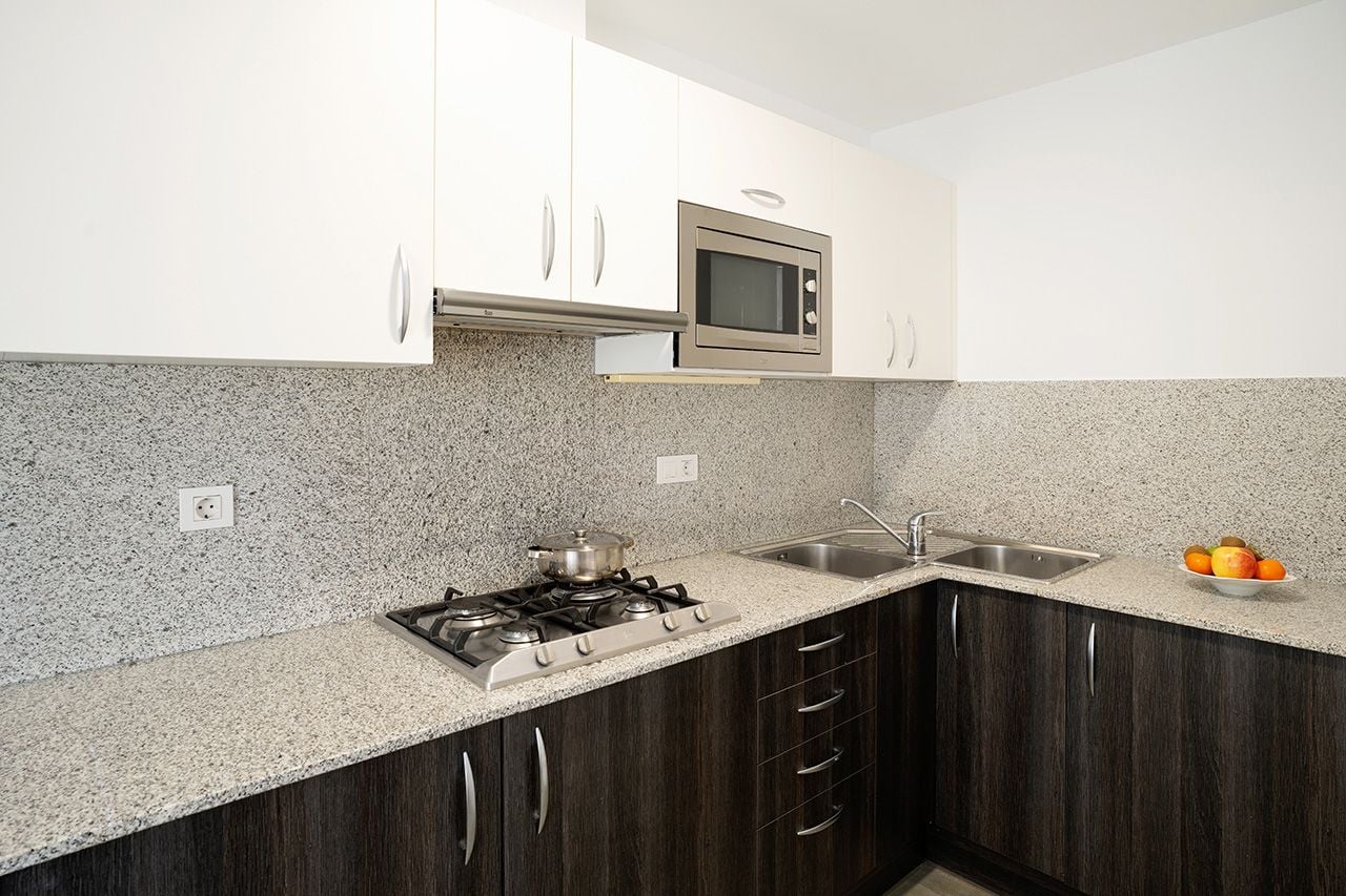 Una cucina con piani di lavoro in granito, fornelli, forno a microonde e pensili in legno scuro.