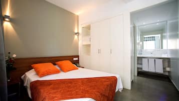 A modern hotel room with a neatly made bed, a large wardrobe, and a bathroom visible through an open door.