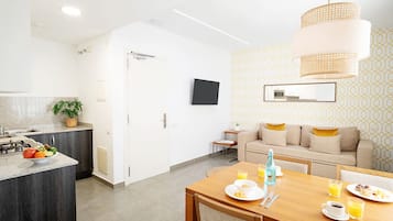 Et moderne køkken med spiseplads, en sofa og et tv ophængt på væggen.