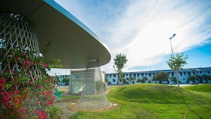 A modern building with a unique geometric design, a grassy area with pink flowers, and a clear sky. - Ona Living Barcelona (L'Hospitalet de Llobregat)