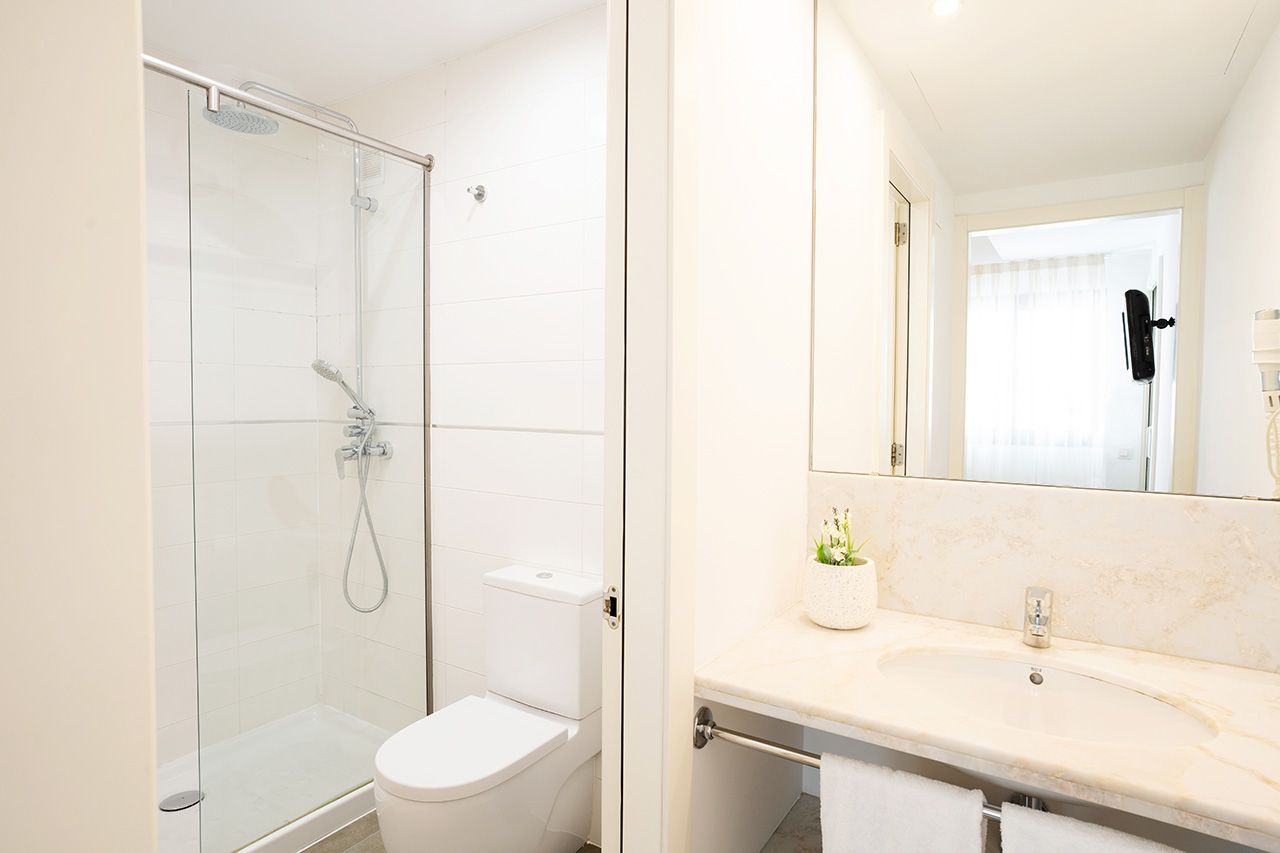 Un baño moderno con ducha envuelta en vidrio, inodoro blanco y lavamanos de mármol con espejo.