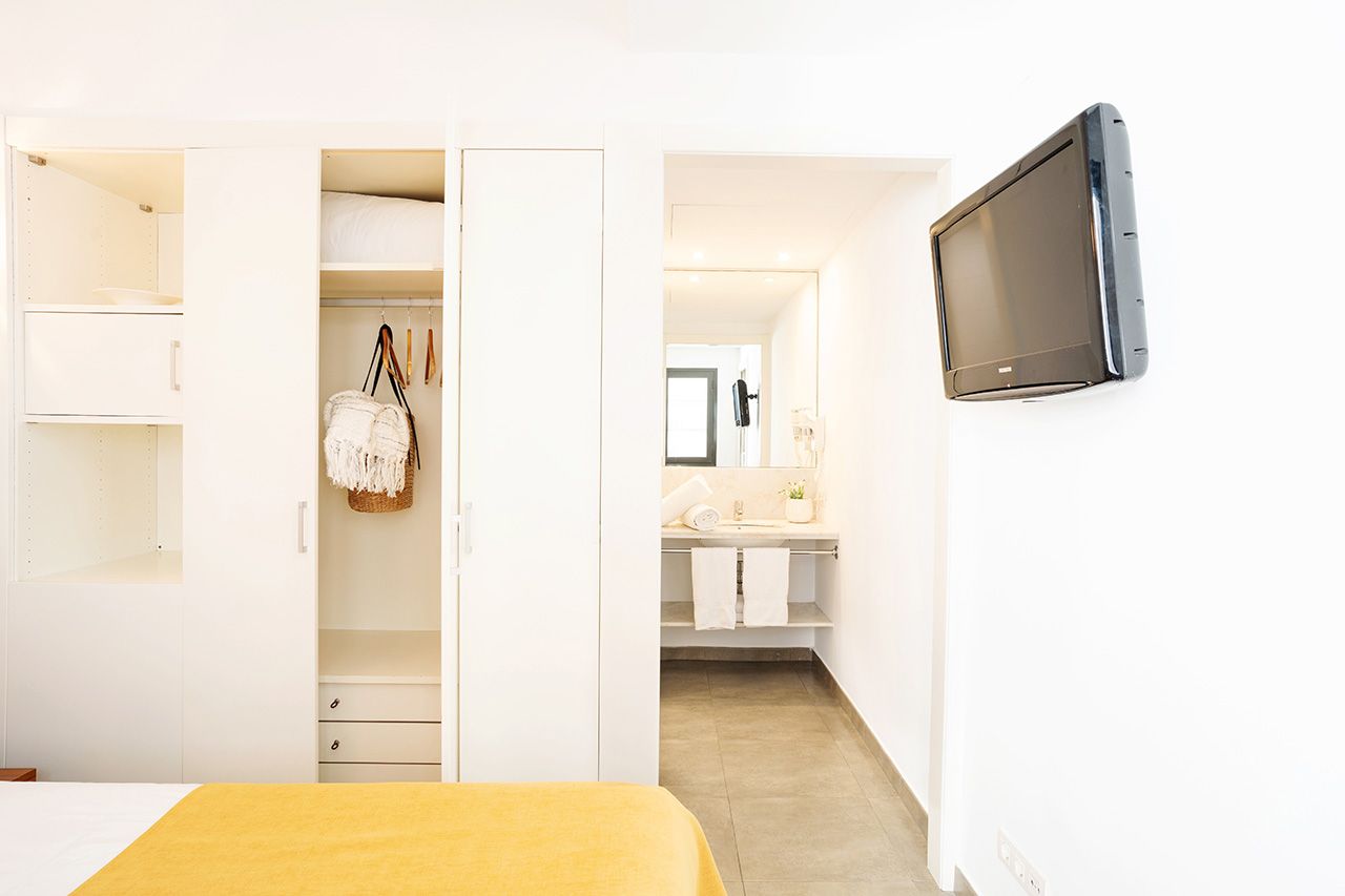 Un dormitorio con cama, armario, televisor y baño visible a través de una puerta abierta.