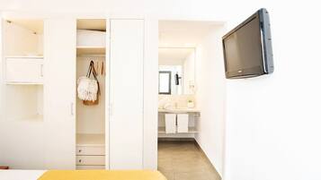 Un dormitorio con cama, armario, televisor y baño visible a través de una puerta abierta.