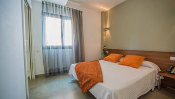 A bedroom with a bed, curtains, a bedside table, and a wall-mounted light.