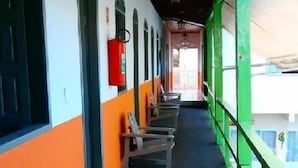 A corridor with chairs and tables, a red fire extinguisher, and a view of buildings outside. - Hotel Pousada Imperial (Porto Seguro)
