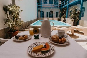 A breakfast setup with plates of food, a coffee pot, and a pool in the background. - Hotel Pousada Imperial (Porto Seguro)