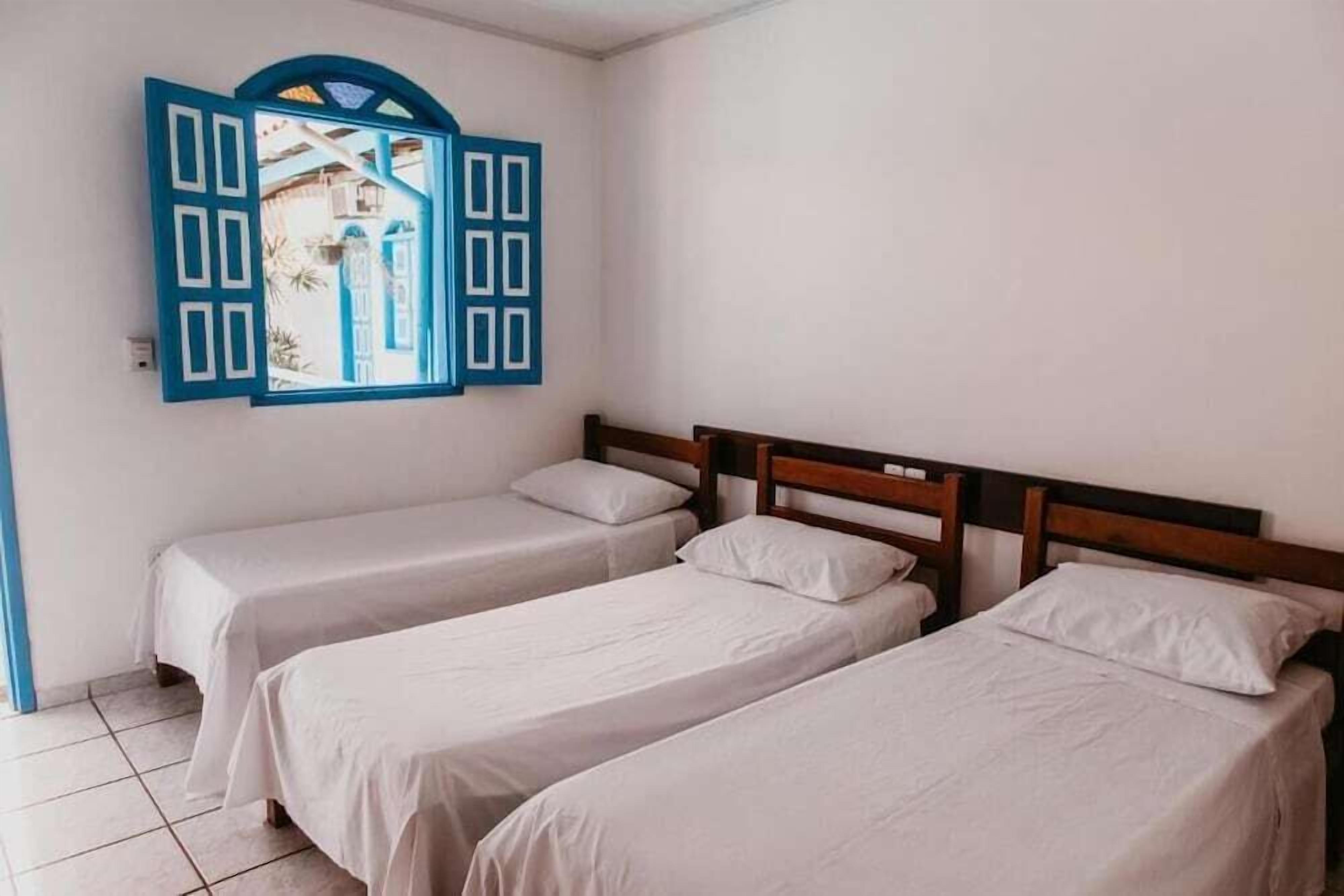 A room with two single beds, a wooden headboard, and a blue-framed window with a view of buildings.