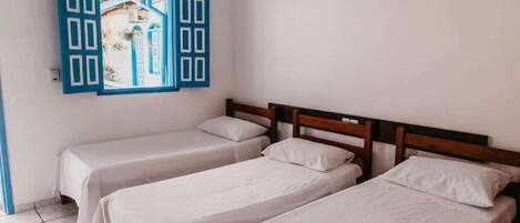 A room with two single beds, a wooden headboard, and a blue-framed window with a view of buildings.