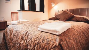 A neatly made bed with a patterned bedspread, a bedside lamp, and a chair with a towel on it. - Cain Valley Hotel (Llanfyllin)