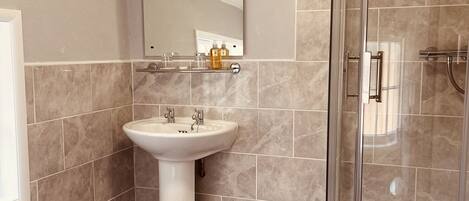 A bathroom with a sink, mirror, shower, and wooden flooring.