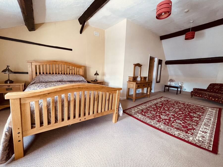 A bedroom with a wooden bed, a nightstand, a dresser, a mirror, a red patterned rug, and a sofa.
