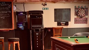 A billiards room with a pool table, stools, a dartboard, and a jukebox. - Cain Valley Hotel (Llanfyllin)