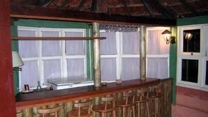 Ein rustikaler Barbereich mit Holzhockern und einer Bar, mit einer grünen Wand und einem Fenster mit Vorhängen.