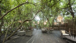 An outdoor wooden deck with wicker furniture and hanging lanterns, surrounded by dense trees. - BALQUISSE Heritage Hotel (Jimbaran)