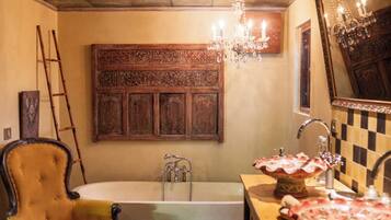 Un baño con bañera, tocador de madera con espejo, candelabro y una silla antigua.