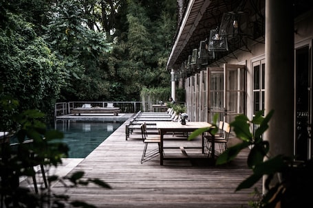 A wooden deck with tables and chairs overlooking a pool, surrounded by lush greenery.