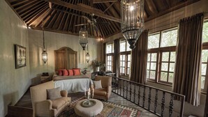 A bedroom with a large bed, a sofa, a small ottoman, and a patterned rug. - BALQUISSE Heritage Hotel (Jimbaran)