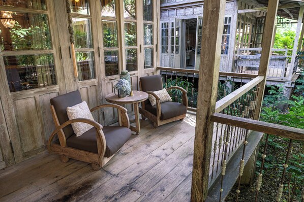 A wooden deck with two chairs and a small table, surrounded by large windows and a wooden railing. - BALQUISSE Heritage Hotel (Jimbaran)