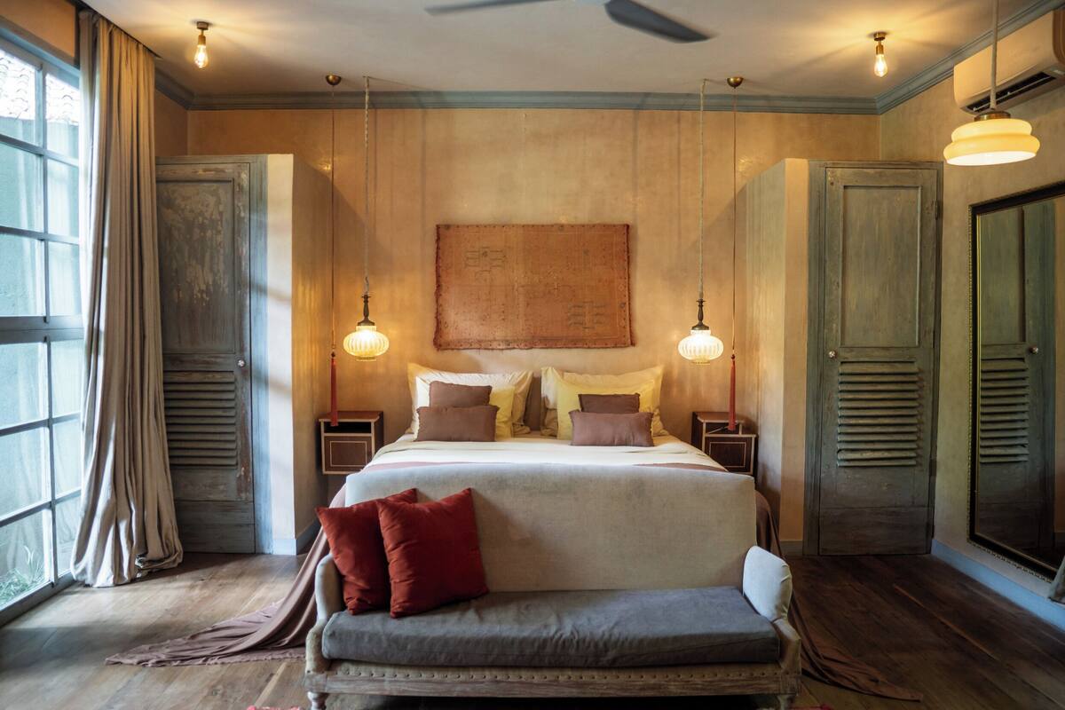 A large bed with multiple pillows, a bench, and two bedside tables with lamps.