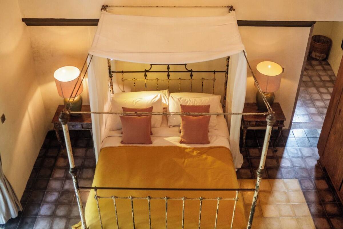 A bedroom with a four-poster bed, a chandelier, and a bedside table with a lamp.