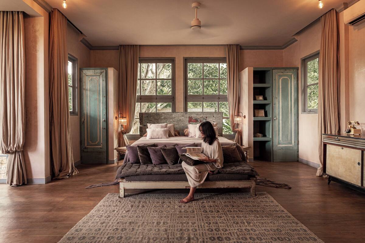 A bedroom with a large bed, a nightstand, a dresser, and a window with curtains.