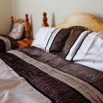 A neatly made bed with a striped bedspread and pillows, a wooden headboard, and a nightstand with a lamp.