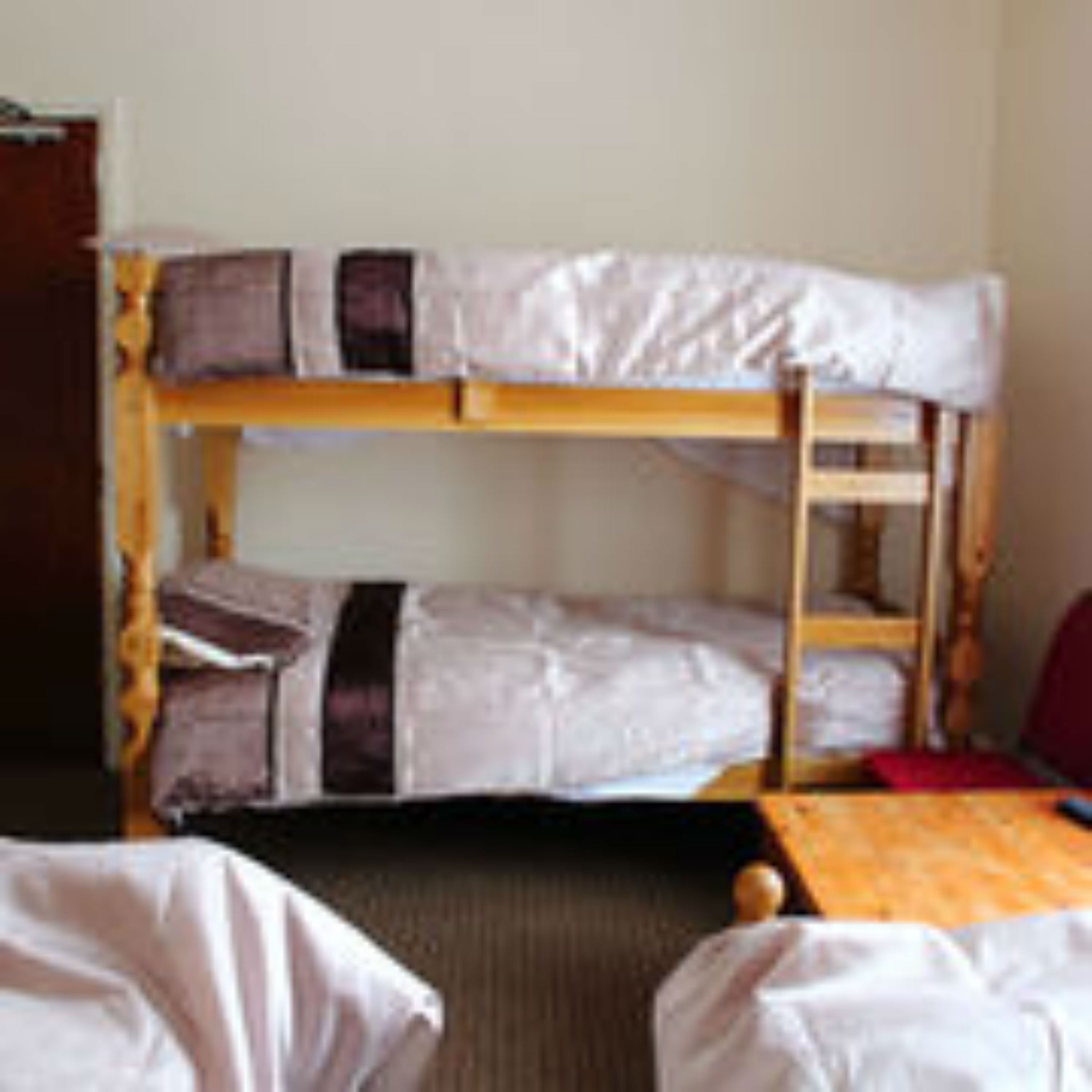 A bunk bed room with a wooden frame, a mattress on the top bunk, and a blanket on the bottom bunk.