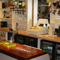 A bar area with a cash register, shelves with bottles, and a refrigerator.