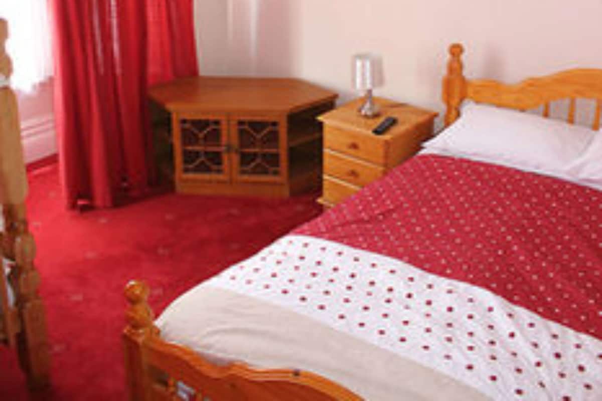 Een slaapkamer met een houten bed, een nachtkastje, een dressoir en een kroonluchter.