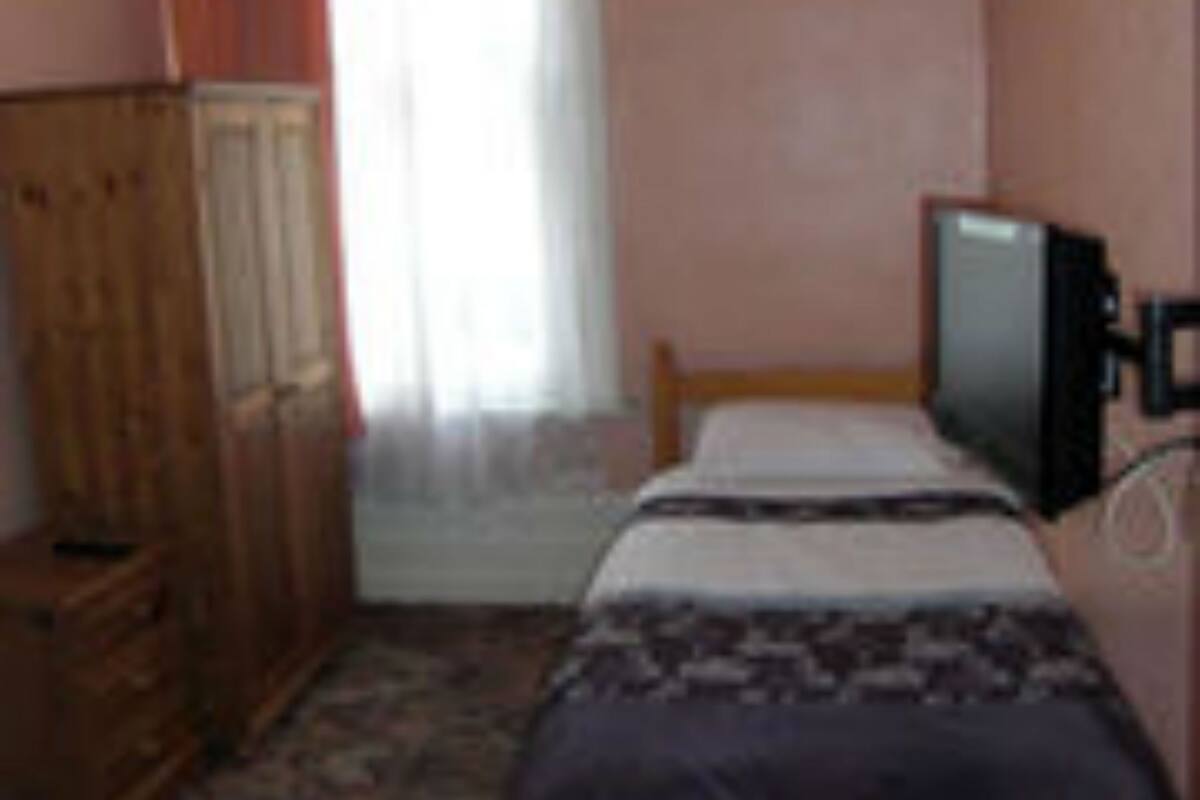Een kamer met een bed, een televisie op een standaard, een kledingkast en een raam met gordijnen.