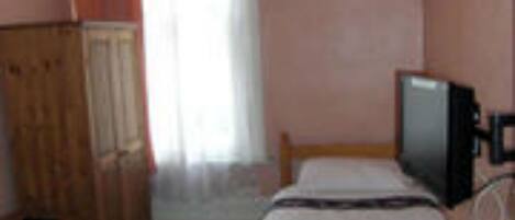 A room with a bed, a television on a stand, a wardrobe, and a window with curtains.