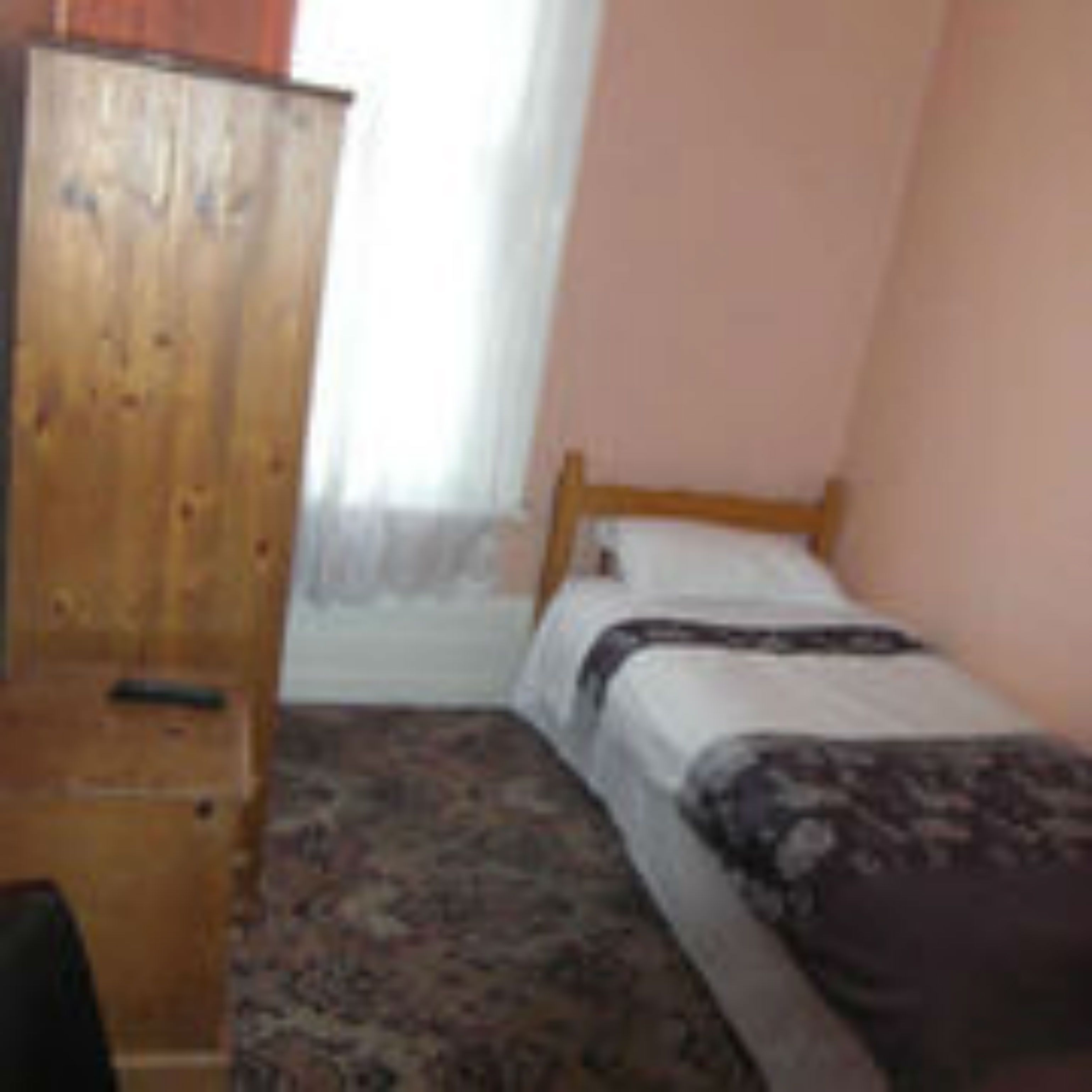 Una camera piccola con un letto singolo, un armadio in legno, un comodino e una tappeto decorato.